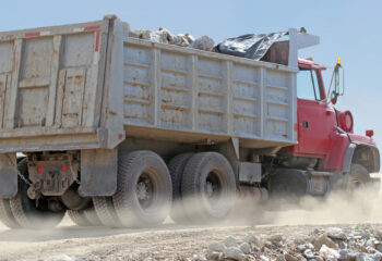 red dump truck transporting boulders on a dusty construction site