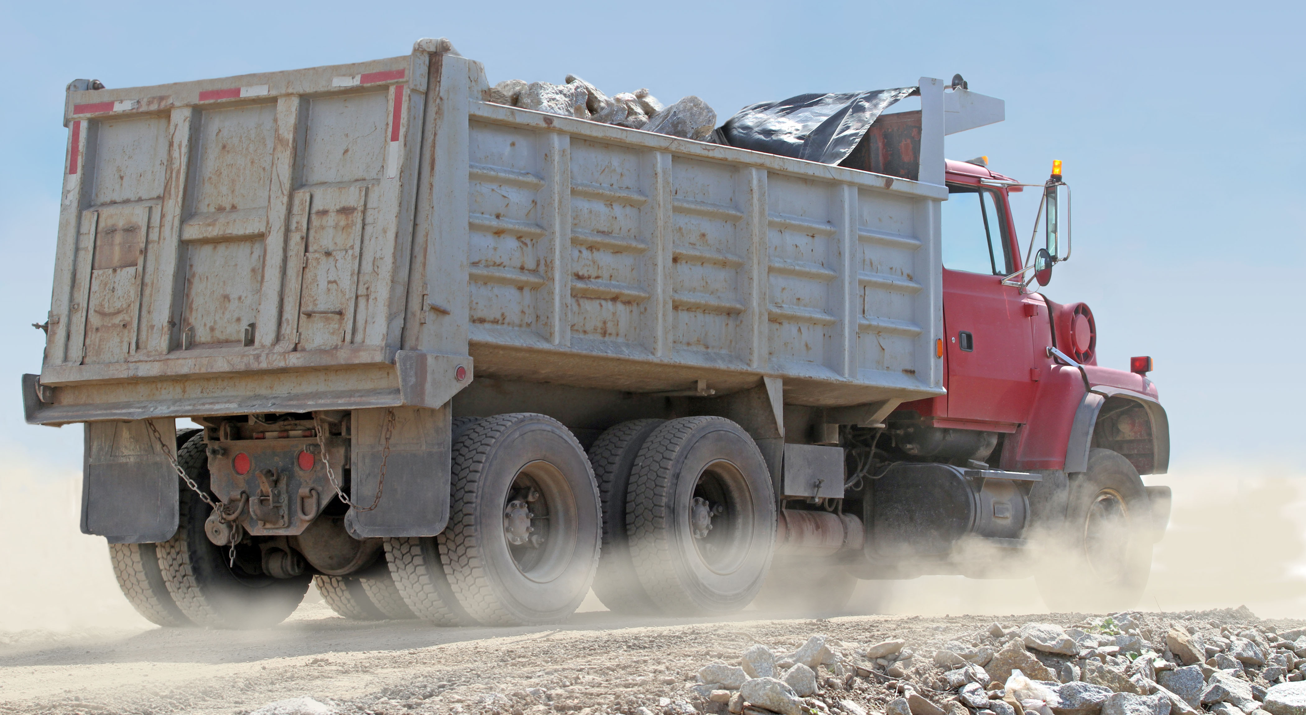 red dump truck transporting boulders on a dusty construction site