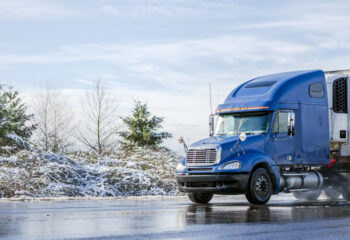 blue semi-truck being driven on a slippery road during winter