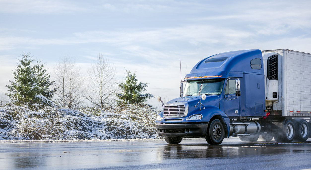 blue semi-truck being driven on a slippery road during winter