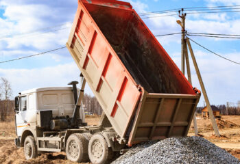 construction gravel unloaded by an orange dump truck on a vacant lot