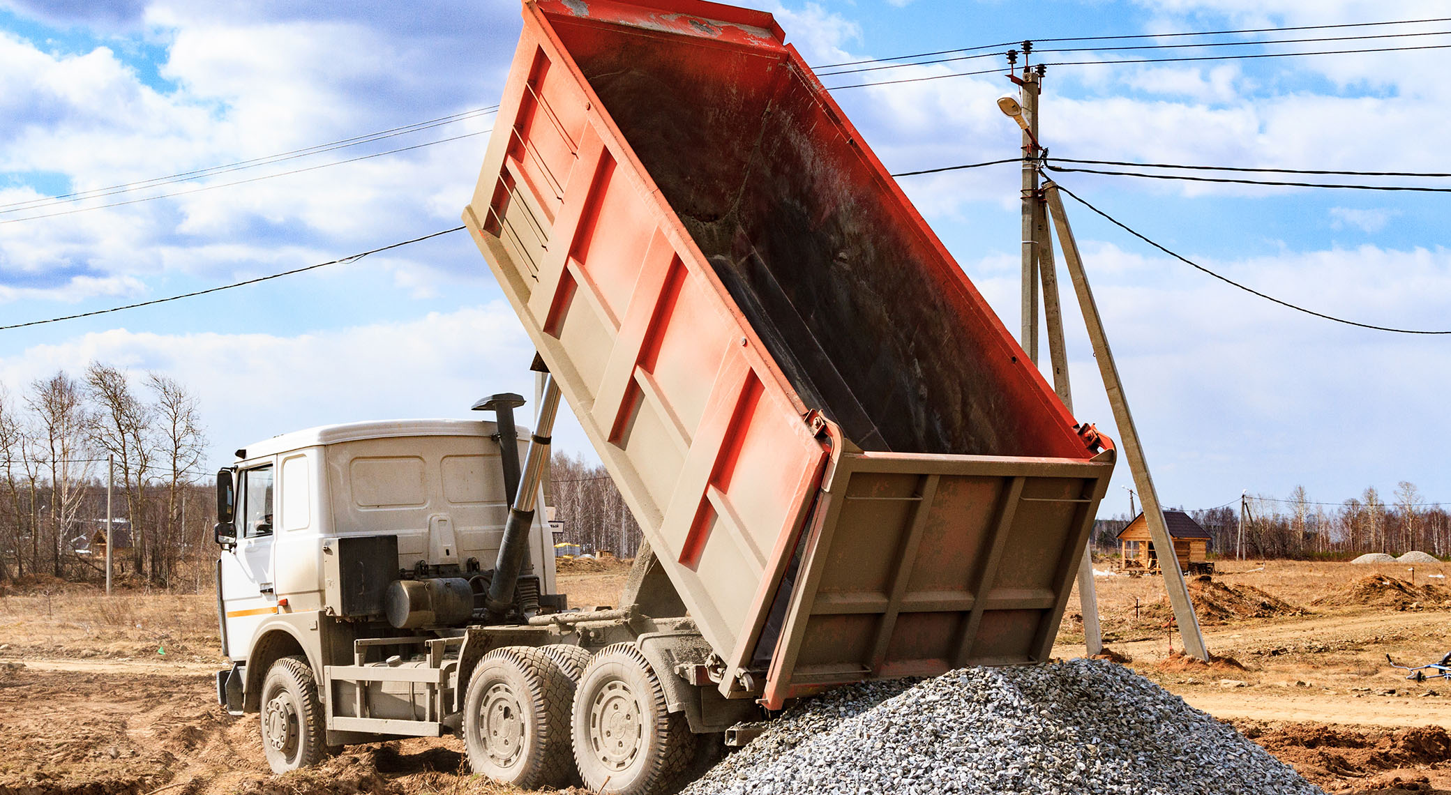 construction gravel unloaded by an orange dump truck on a vacant lot