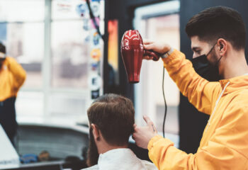 barber wearing a face mask during a pandemic while blow drying customer's hair