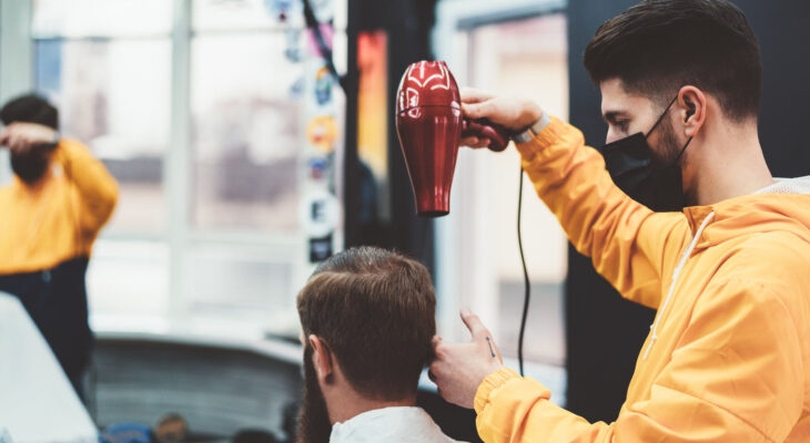 barber wearing a face mask during a pandemic while blow drying customer's hair