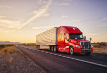 red semi-truck driving on a road during sunset