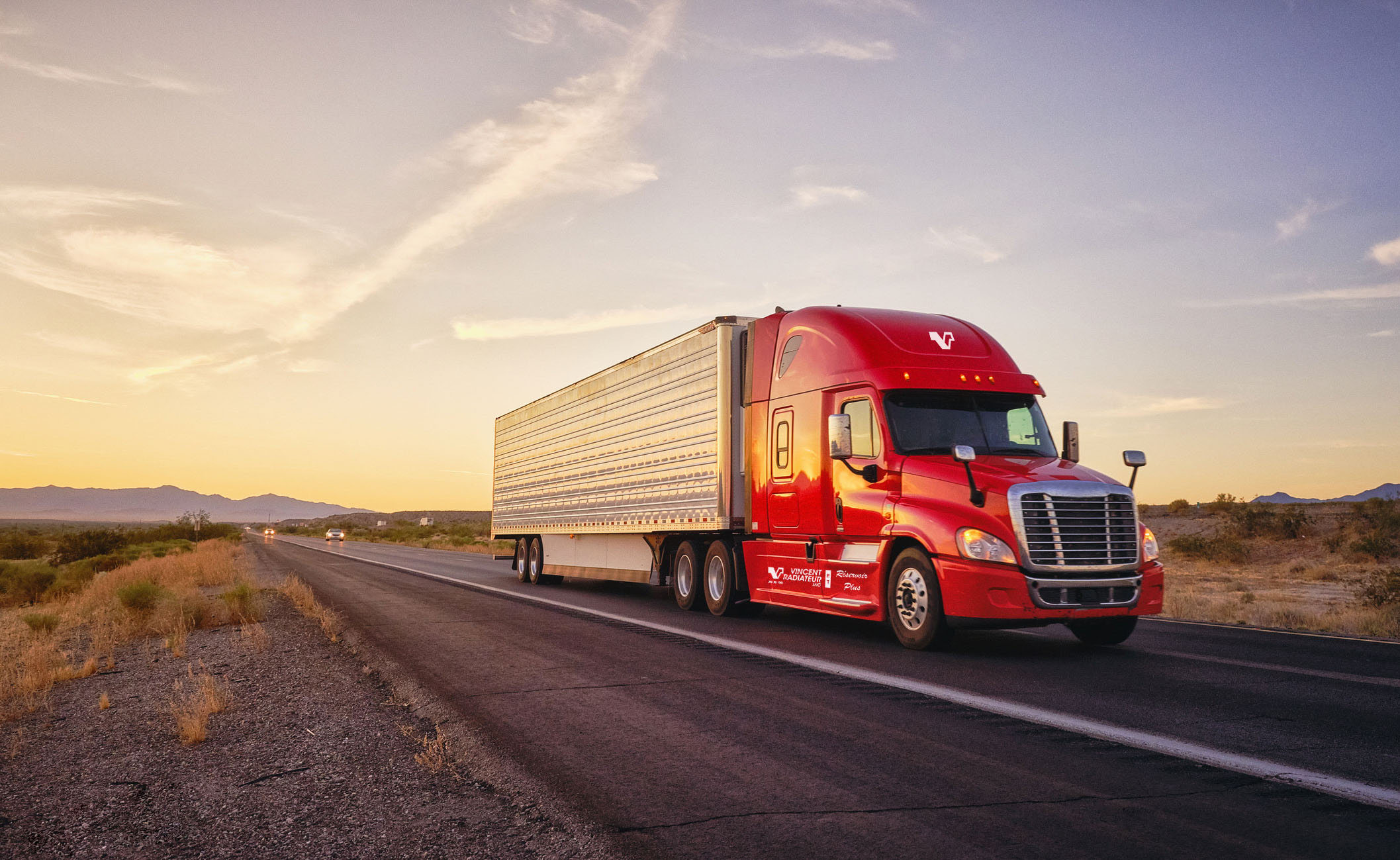 red semi-truck driving on a road during sunset