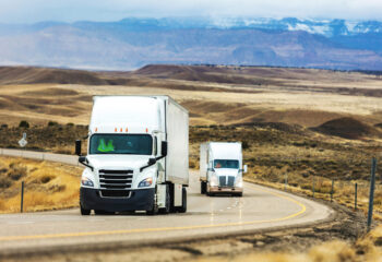 two day cab trucks being driven on a road