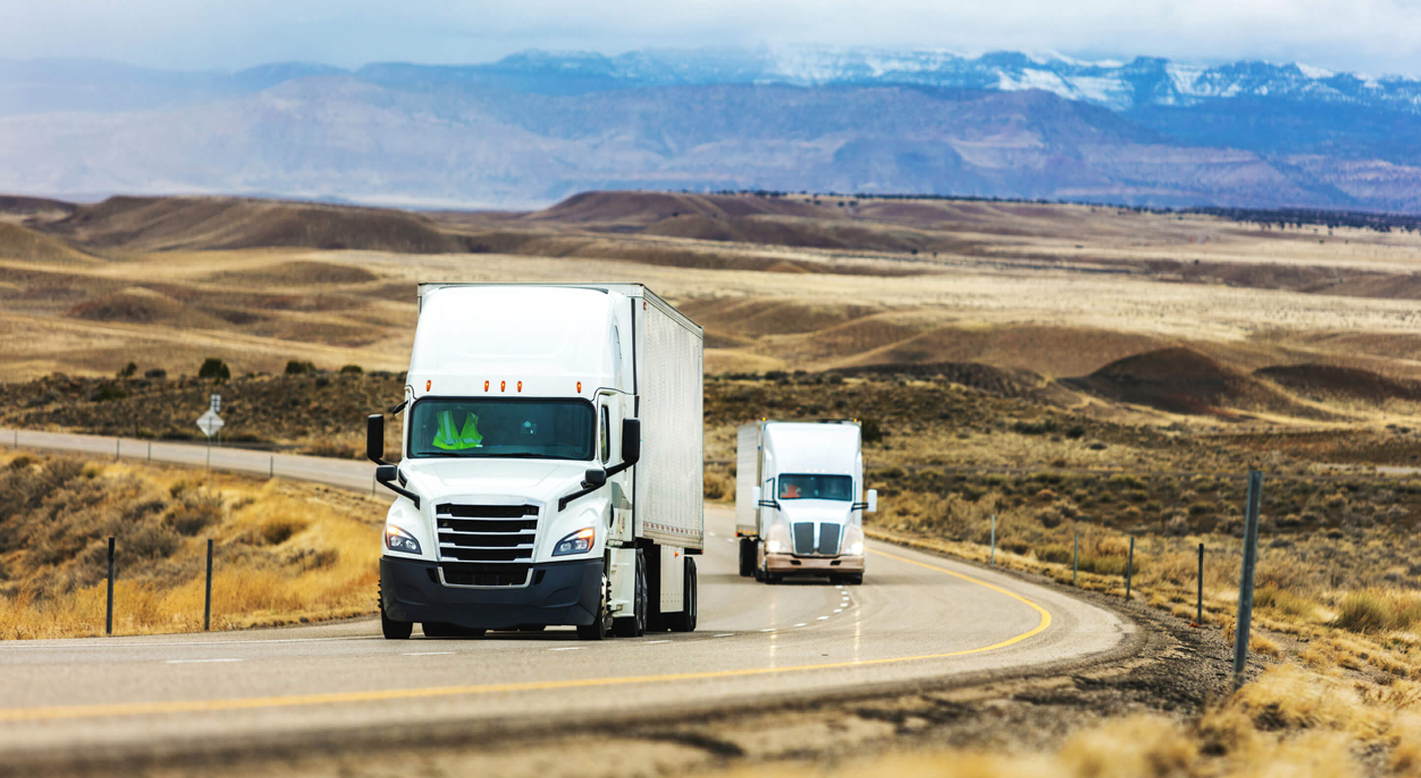 two day cab trucks being driven on a road