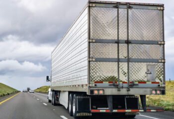 semi trailer truck with metallic trailer being driven on a light traffic road