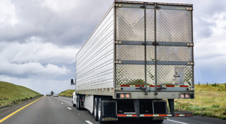 semi trailer truck with metallic trailer being driven on a light traffic road