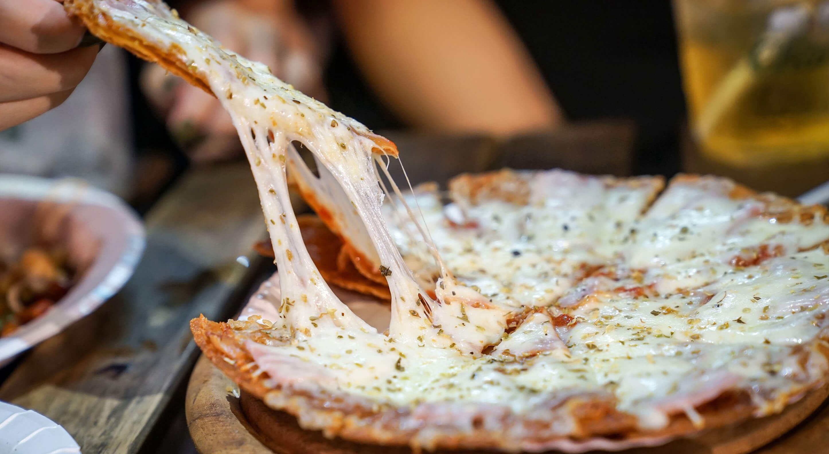 person's hand taking a slice of pizza from a pizza plate