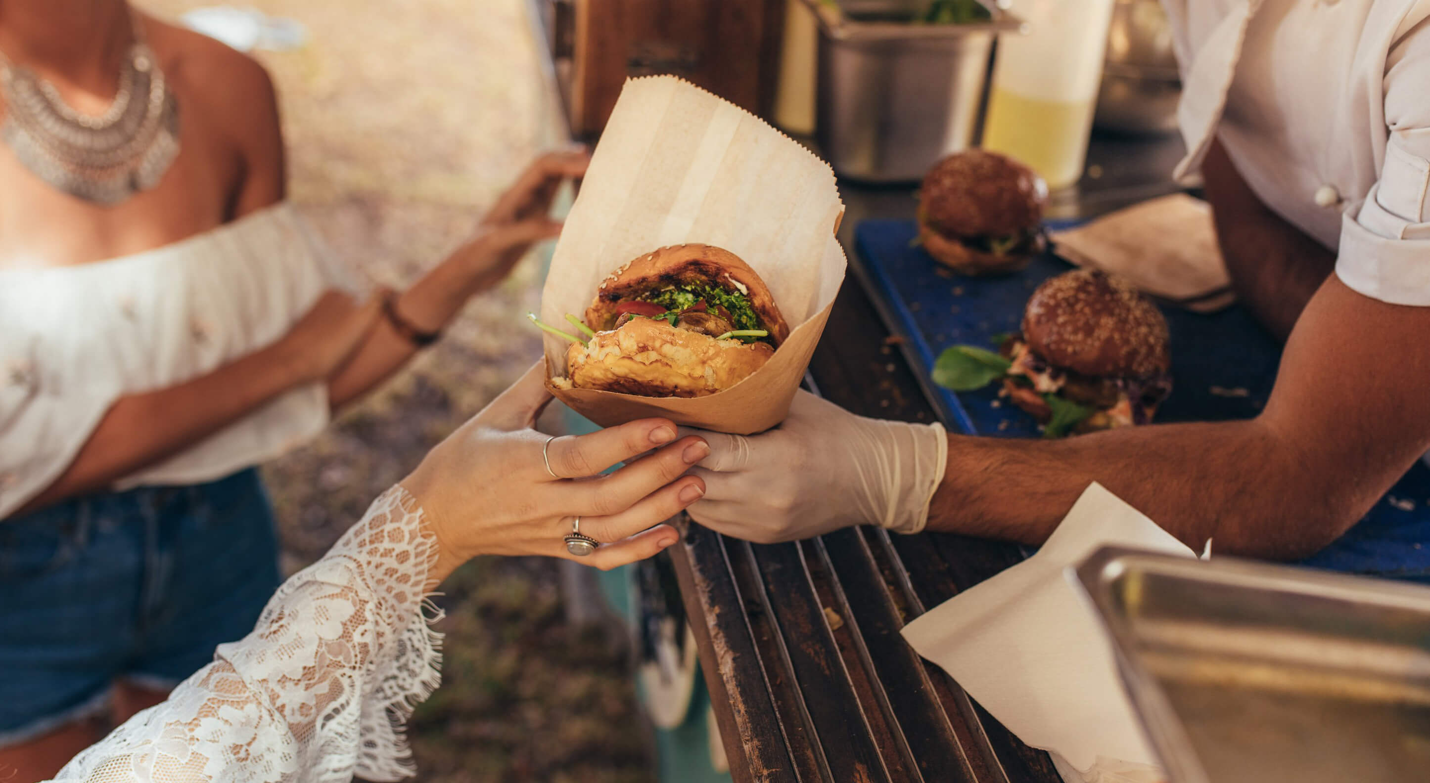 woman's hand receiving a burger from a catering food truck owner
