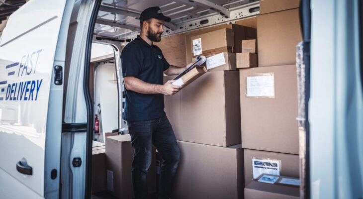 a young delivery man checking a list of packages inside a step van