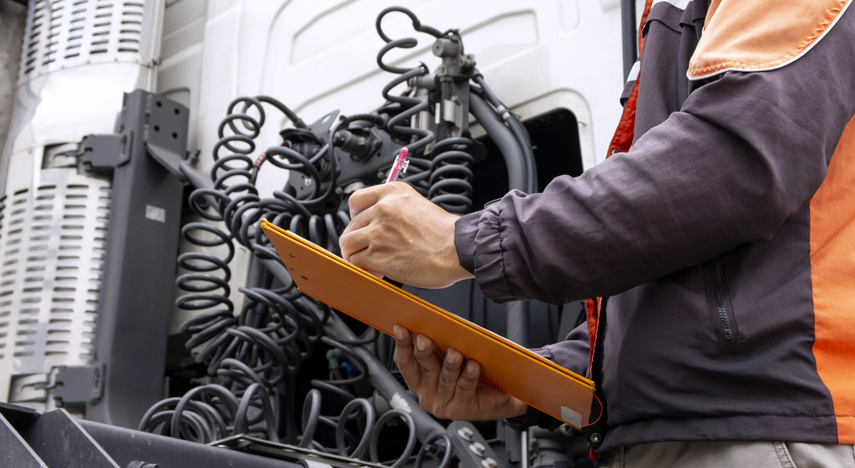 truck driver holding a clipboard while inspecting the engine of a day cab truck for daily safetycheck