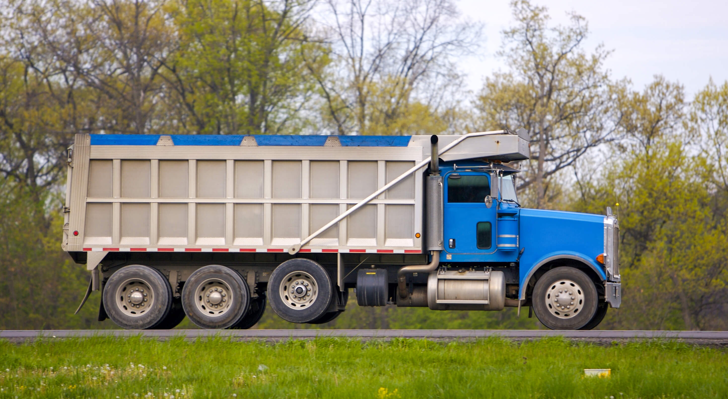 blue tarped dump truck in a grassy road
