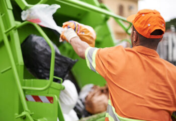 garbage collection worker in front of a green garbage dump truck collecting garbage