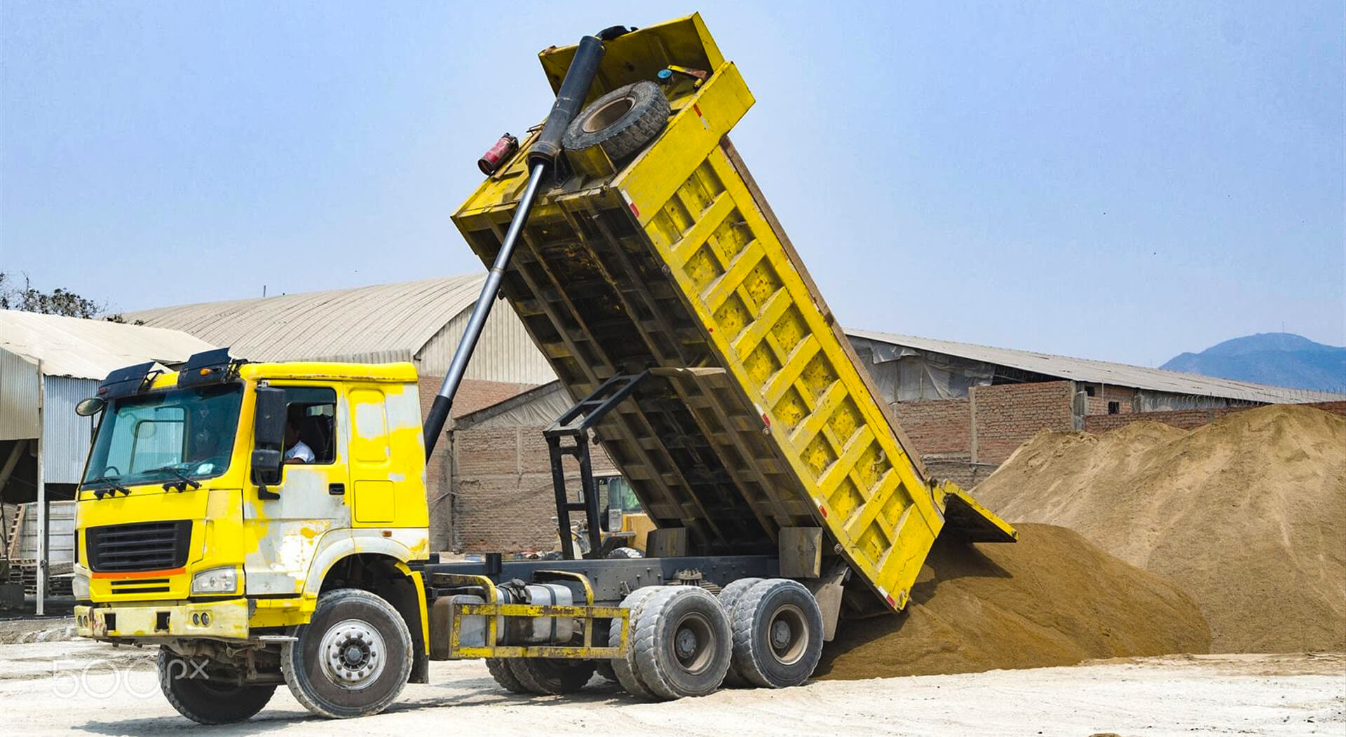 yellow dump truck delivering a load of dirt for a project at a construction site