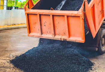 orange dump truck unloads fresh asphalt into the spreader on a road in the city