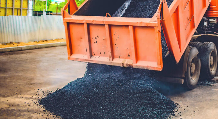 orange dump truck unloads fresh asphalt into the spreader on a road in the city