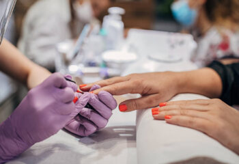 beautician with face shield and mask giving manicure to female customer at beauty salon