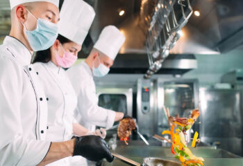 chefs in protective masks and gloves prepare food in a ghost kitchen