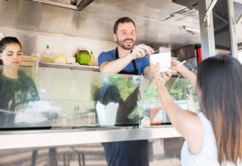 food truck server in a food truck handing over a box with oriental food to a female diner