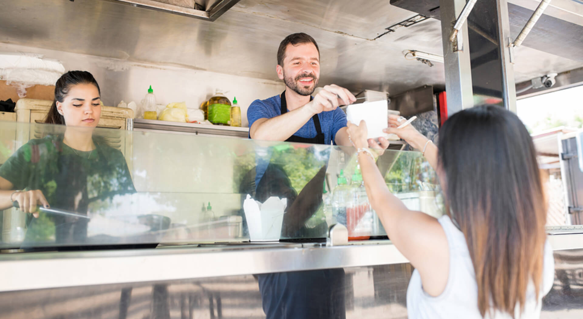 food truck server in a food truck handing over a box with oriental food to a female diner