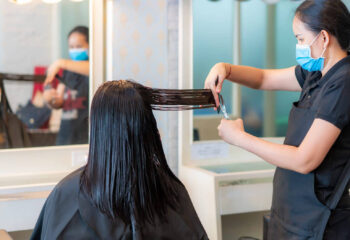 hairdresser trimming an asian woman's black hair with scissors in a mobile hair salon