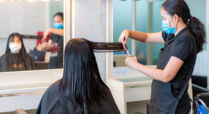 hairdresser trimming an asian woman's black hair with scissors in a mobile hair salon