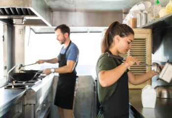 two people cooking and serving oriental food inside a food truck kitchen