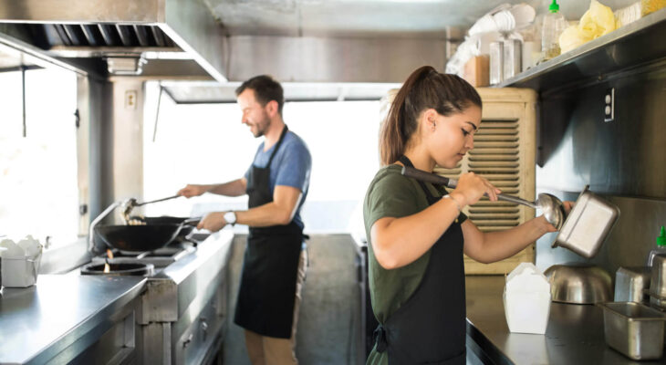 two people cooking and serving oriental food inside a food truck kitchen