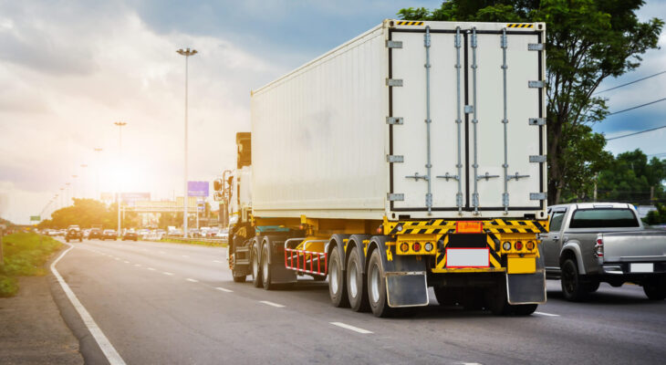 white semi truck driving on a road during summer