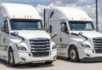 two white Freightliner sleeper trucks lined up for sale