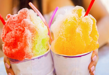 two colorful shaved ice treat held by a woman on a hot summer day