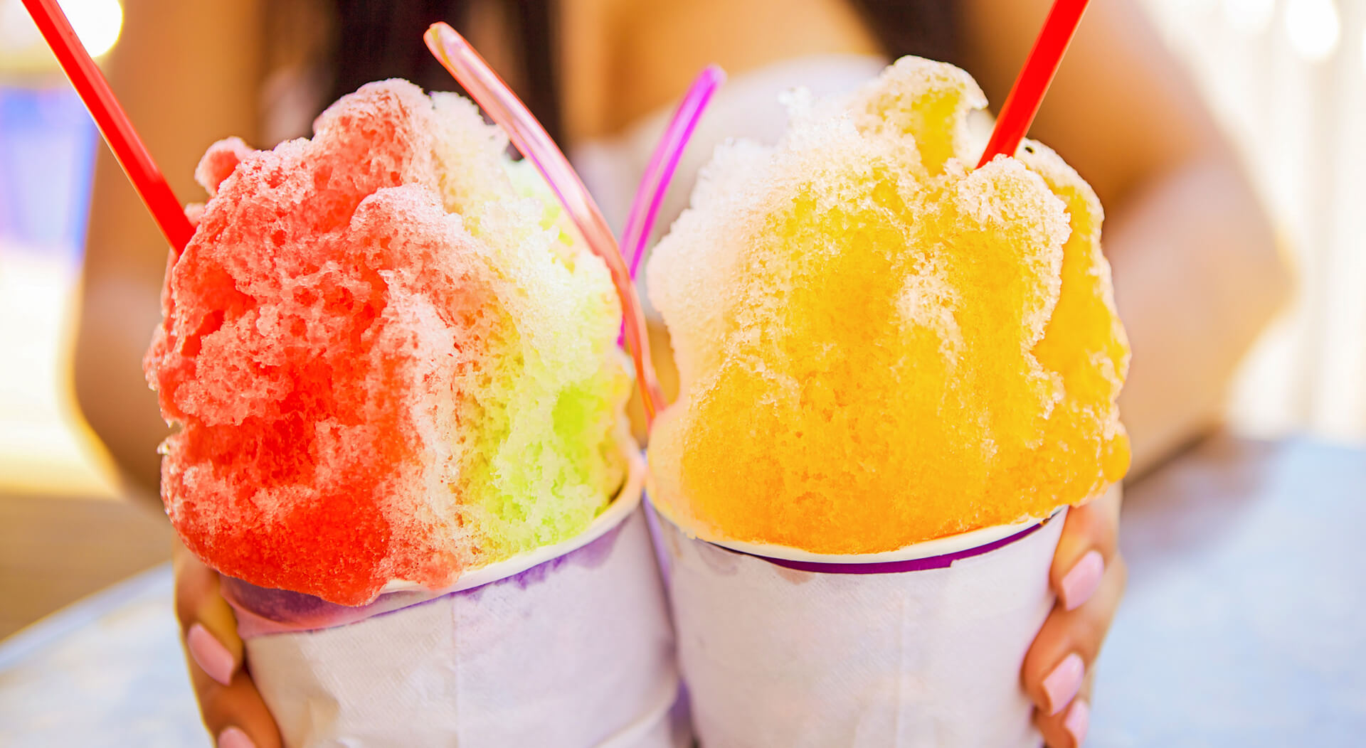two colorful shaved ice treat held by a woman on a hot summer day