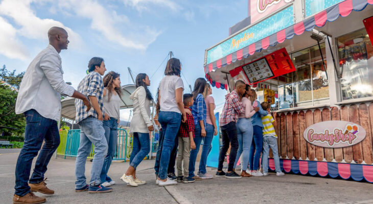 happy people at a funfair lined up to buy food at a candy shop