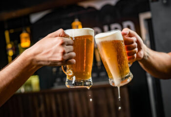 two people in front of a food truck toasting with mugs full of beer