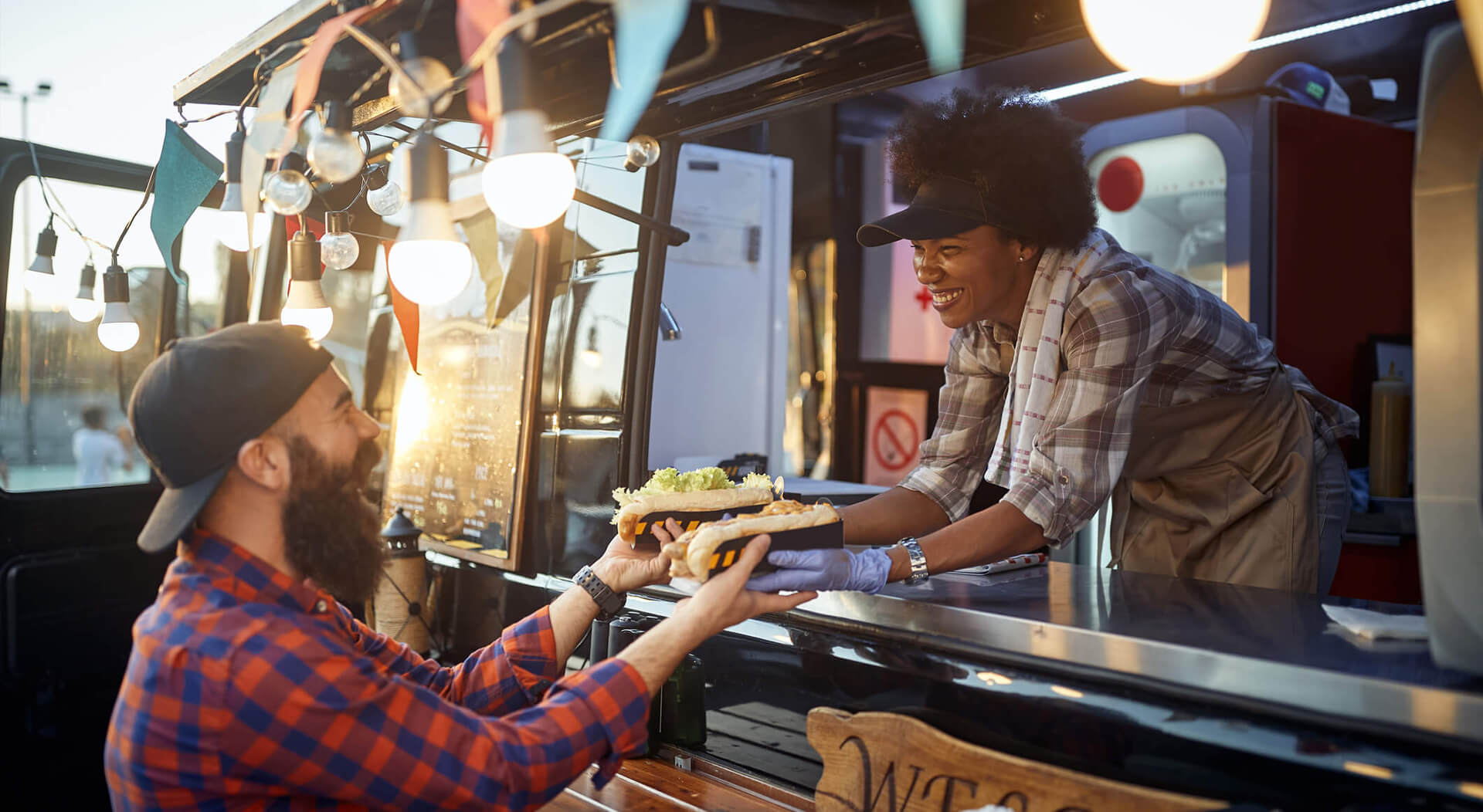 young man taking two sandwiches from polite female food truck employee