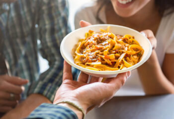 young woman smiling with pleasure while getting pasta that was just ordered at counter of food truck