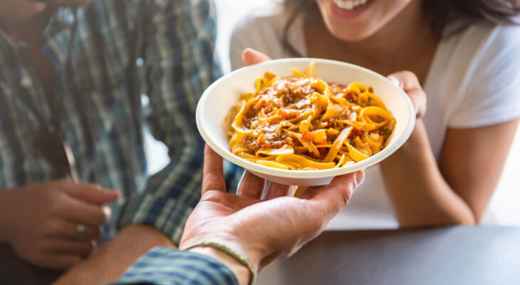 young woman smiling with pleasure while getting pasta that was just ordered at counter of food truck