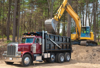 Excavator loading dumper truck with dirt at construction site