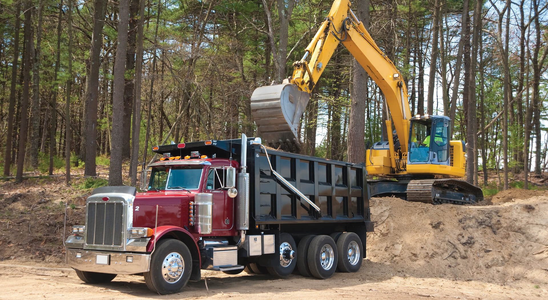 Excavator loading dumper truck with dirt at construction site