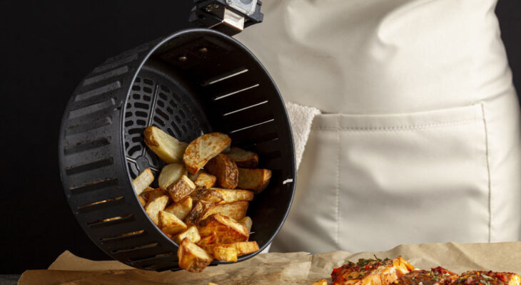 a chef is dumping fresh made fried potato chunks on a piece of baking paper which has three oven roasted marinated salmon fillet with basil and pepper on top