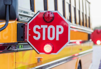 A yellow school bus stopped on the side of the road with stop signs out and flashing