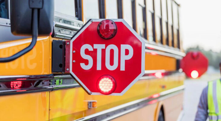 A yellow school bus stopped on the side of the road with stop signs out and flashing