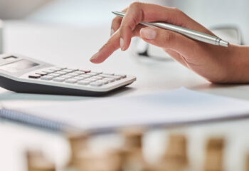 person's hand holding a ballpen while using a calculator