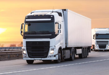 two white high mileage trucks on a highway at sunset