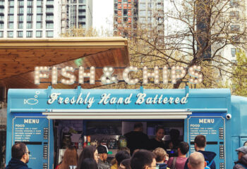 a blue food truck selling fish & chips parked in a populated area