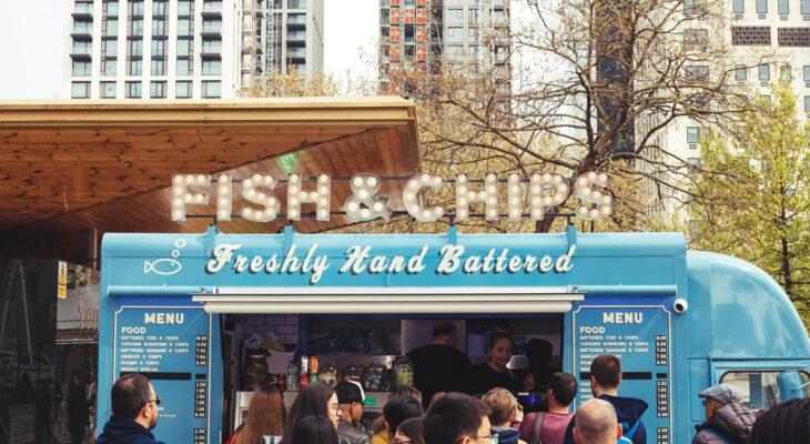 a blue food truck selling fish & chips parked in a populated area