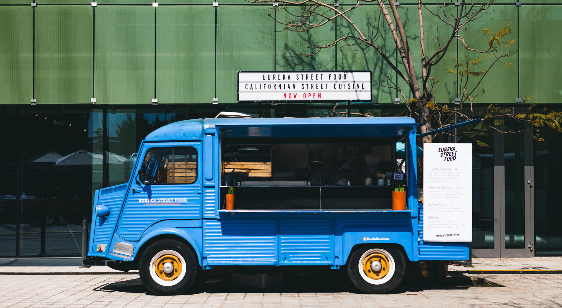 blue food truck parked in front of a green building on a sunny day